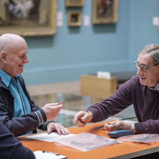 making conversation - a woman two older gentlemen sitting around a table, smiling whilst drawing in a gallery space