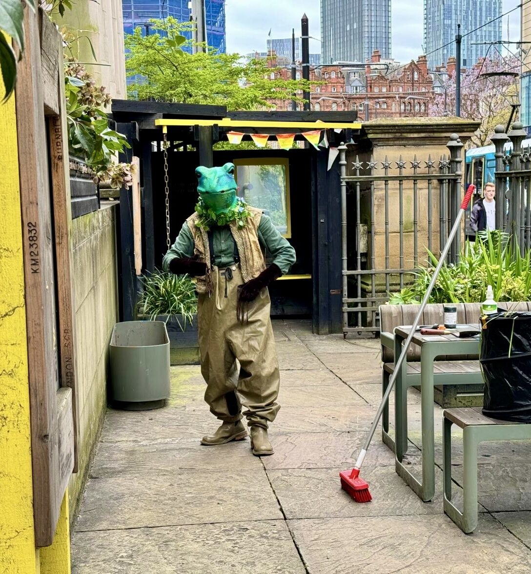 a man in a green frog mask is walking and lceaning the sidewalk