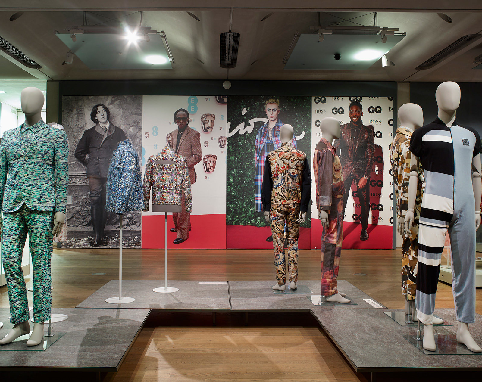 Dandy Style Exhibition view of gallery 13, contemporary suits on mannequins in front of a back ground wall of celebrities who could be considered as modern dandies