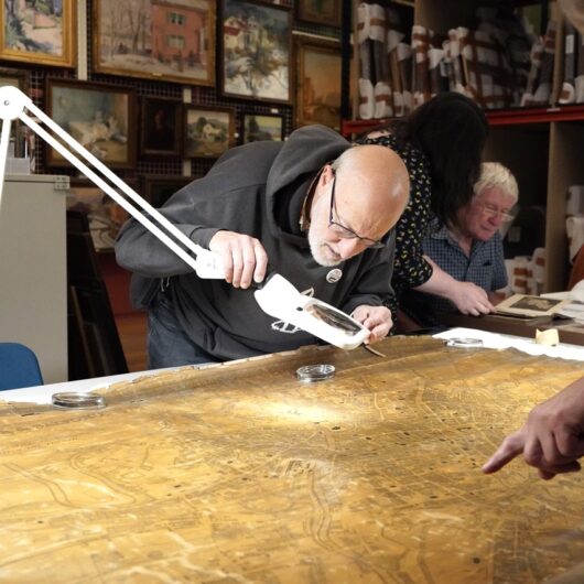 Older gentleman with glasses looking through a magnifying glass at a large antique map