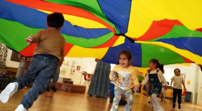 Children playing underneath a colourful parachute