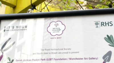 Two hands holding a sign highlights that the RHS and North West in Bloom are presenting an award as a recognition for 