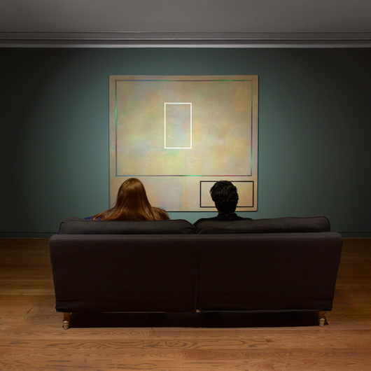 Room to Breathe installation shot- two people sat on a sofa from behind looking at an abstract painting
